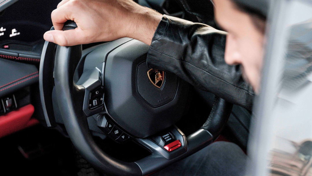 Man with one hand on a black steering wheel of a global car rental