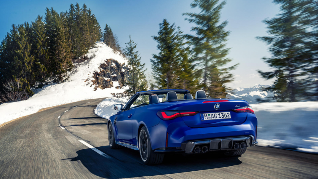 A new 2024 BMW M4 car rental in blue driving down a road with a backdrop of snow and trees