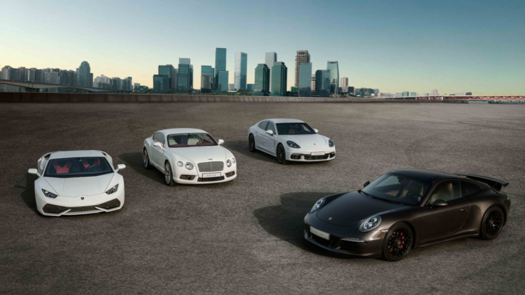 Four high-end sleek cars parked against backdrop of blue city skyline with skyscrapers