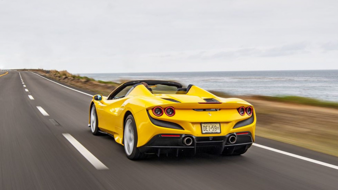 Yellow Ferrari F8 Spider exotic car rental cruising down an open road by the coast