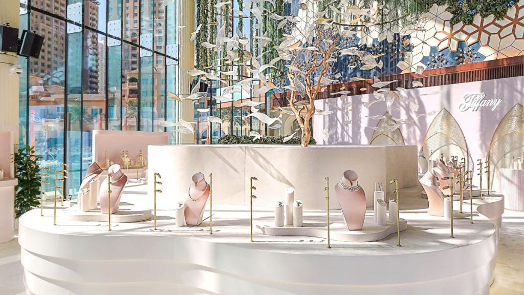 A view of Tiffany & Co's Bird on a Pearl Jewellery collection featuring necklaces and earrings in a bright room with glass and. A large centre-piece tree with fake white birds can be seen